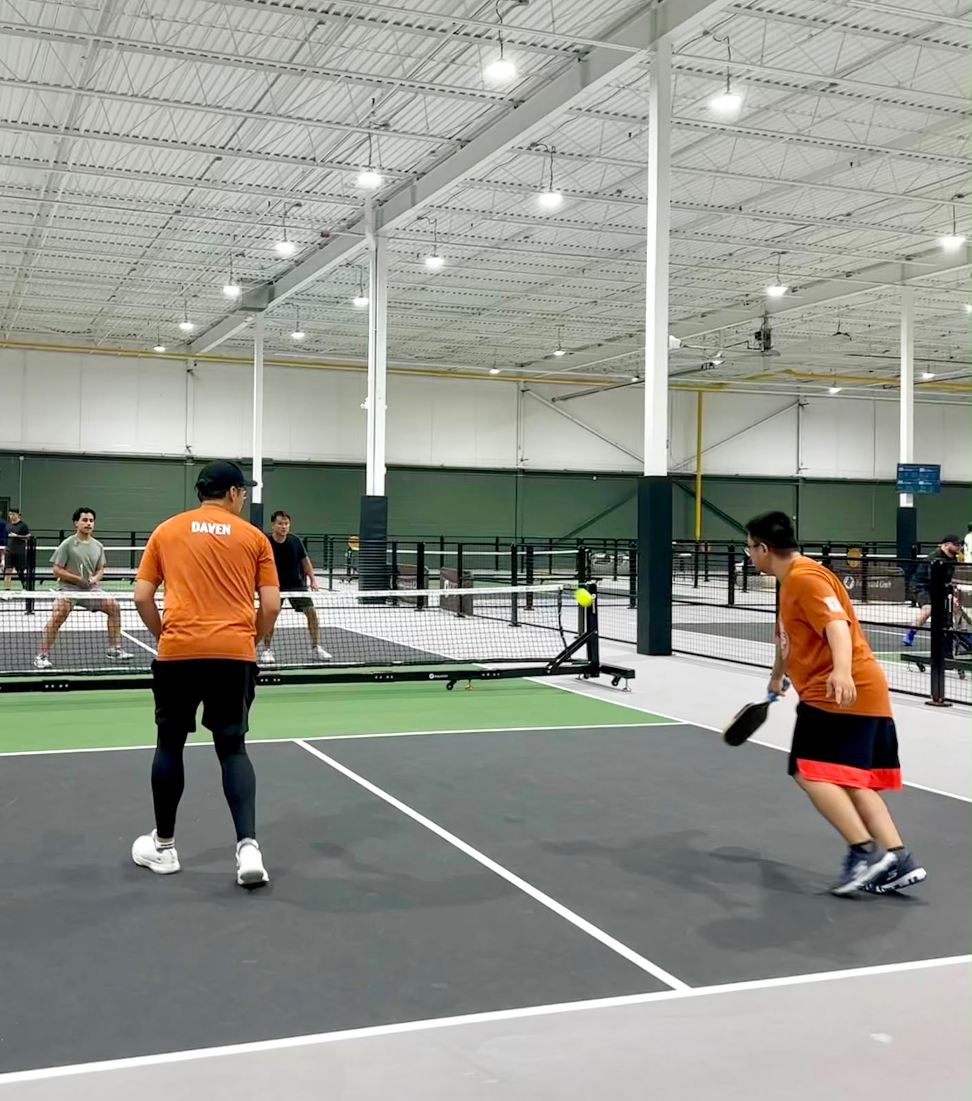 Adrian chasing down a ball with his paddle low while Daven holds the baseline
