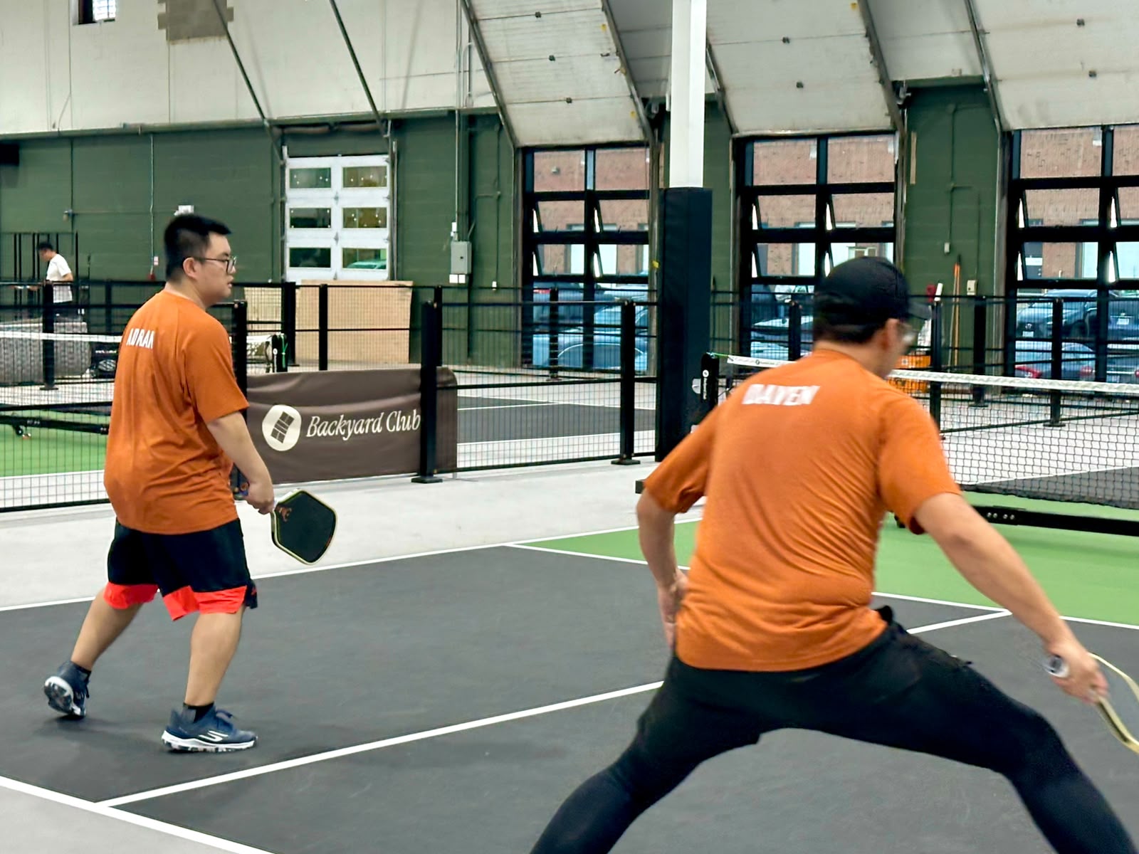 Daven lunging wide for a ball in the foreground, Adrian behind him with his paddle ready