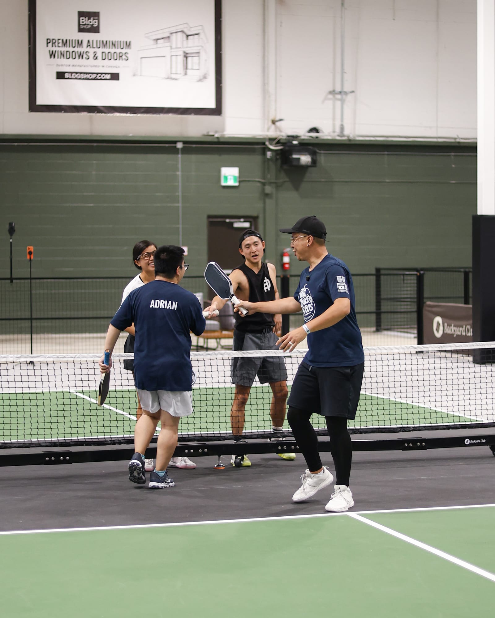 Adrian and Daven shaking hands at the net after a game, Adrian's name across the back of his shirt