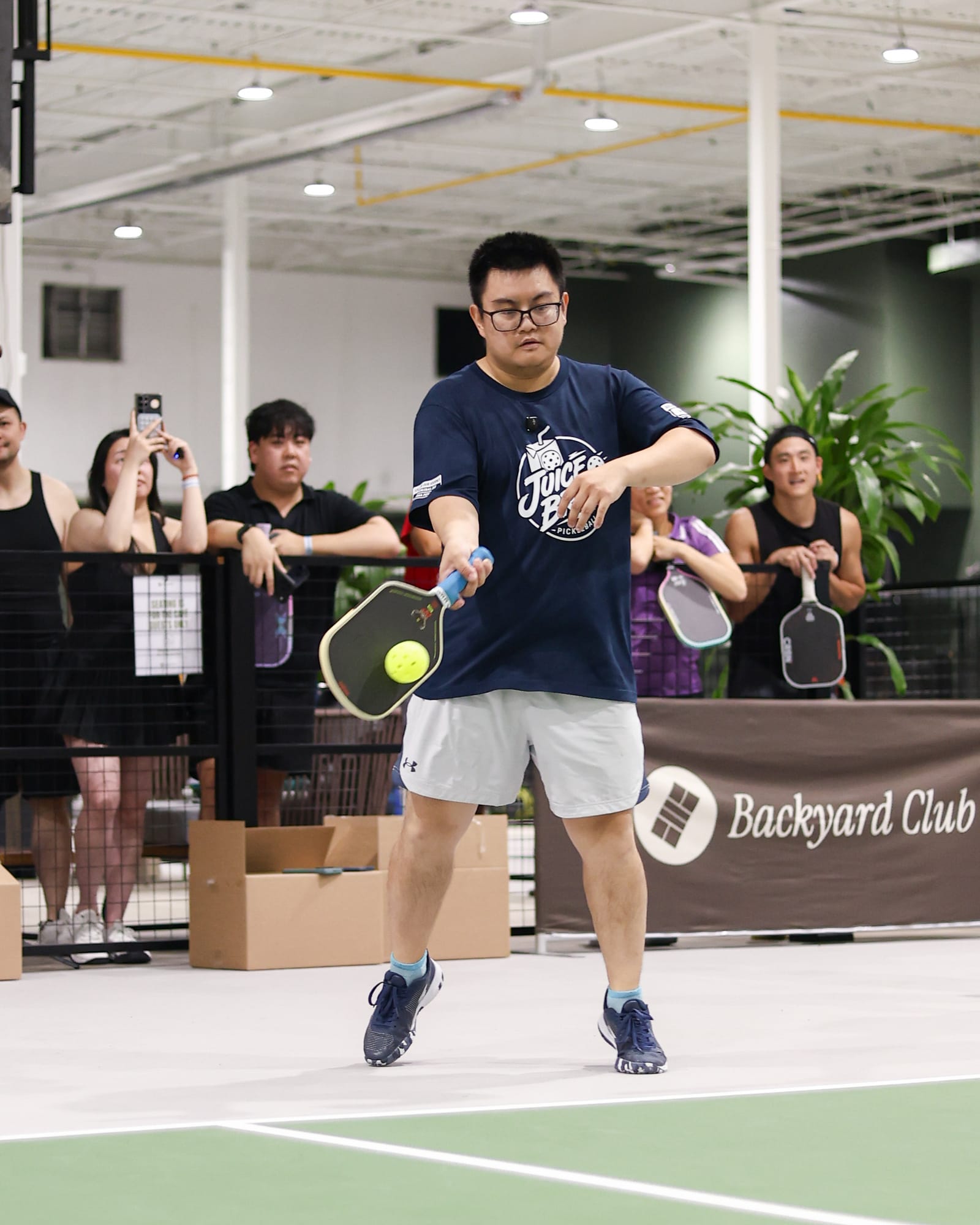 Adrian in glasses and a Juice Bros shirt, about to hit a forehand