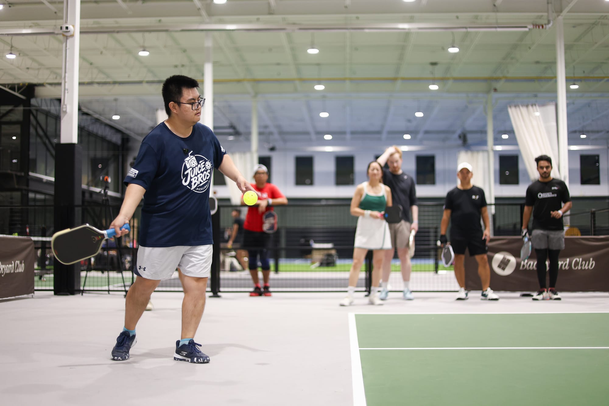 Adrian lining up a serve with the ball in his free hand while other players wait behind him