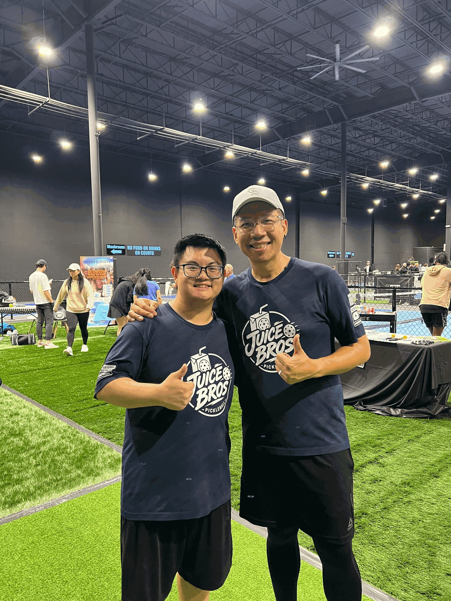 Adrian and Daven in matching Juice Bros shirts, Daven's arm around Adrian's shoulders, both giving a thumbs up